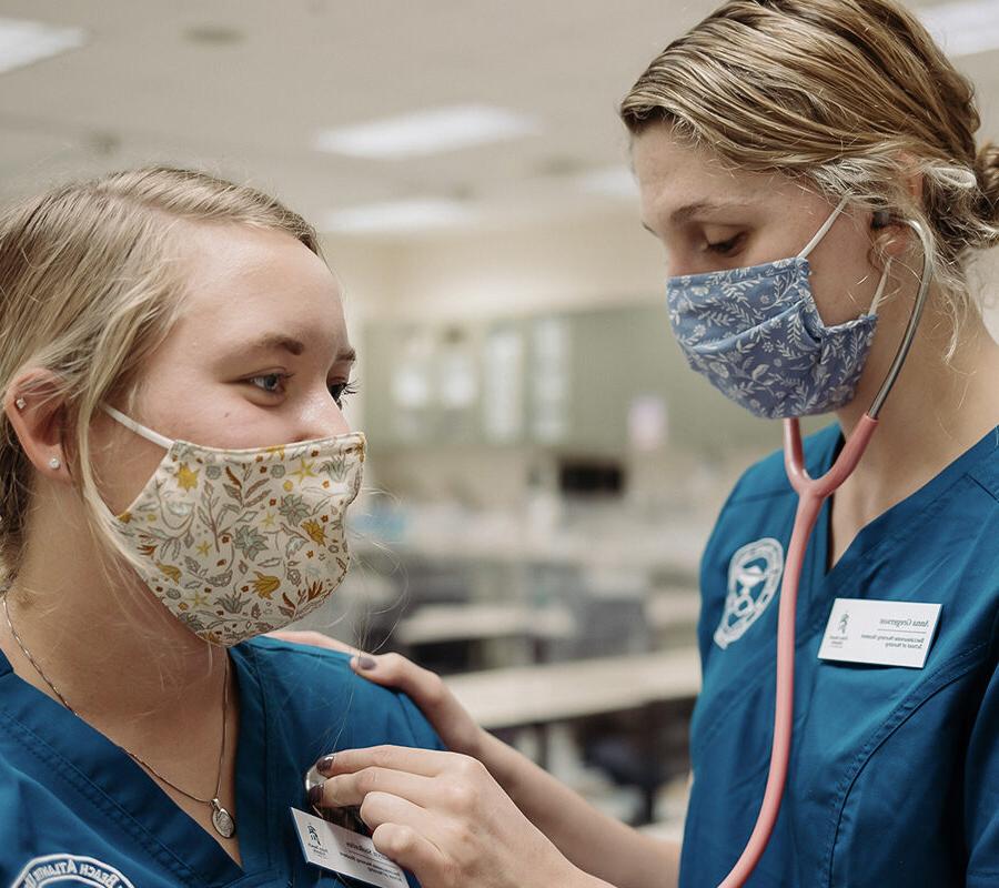 a nursing student listening to the heartbeat of another student through a stethoscope